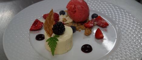 Un plato de postre con una porción de helado, fresas, zarzamoras y una pequeña decoración de hoja.