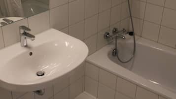 Un baño con lavamanos y bañera blancos, paredes con azulejos y una cabina de ducha de cristal.