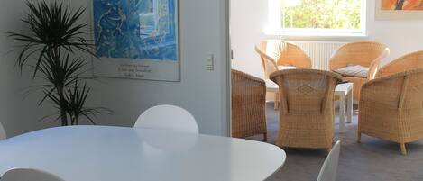Ein modernes Zimmer mit einem weißen Tisch und Stühlen, Korbmöbeln und Kunstwerken an den Wänden.