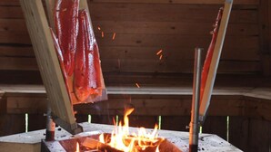 Una estufa de leña con fuego ardiendo en el interior de una cabaña de paredes de madera y una ventana.