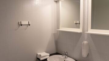 A bathroom with white tiled walls, a white sink, a mirror, and a soap dispenser.
