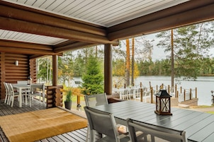 Una terraza de madera con una mesa y sillas, con vistas a un lago con árboles y un muelle.