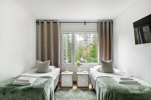 Un dormitorio con dos camas, una ventana con cortinas, una mesita de noche con lámpara y vistas a árboles.