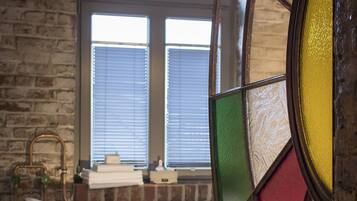 A room with a bathtub, a window with blinds, and a stained glass window.