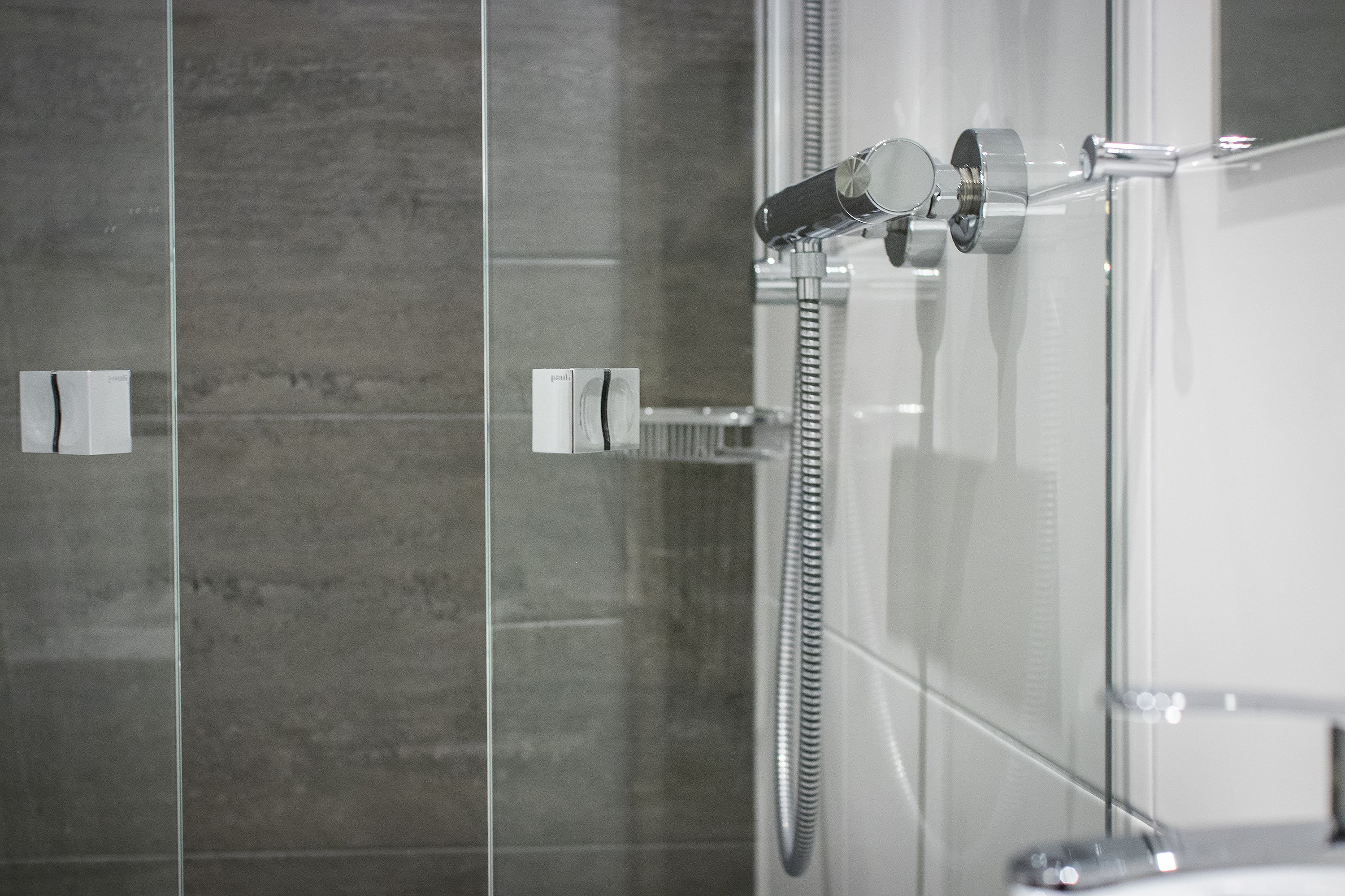 A modern bathroom with a glass shower enclosure, a handheld showerhead, and a visible control panel.
