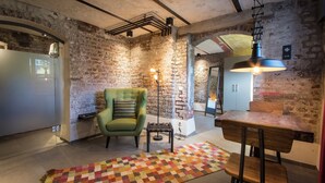 Une cuisine moderne avec un mur en briques, un fauteuil vert, une table à manger en bois et un tapis coloré.
