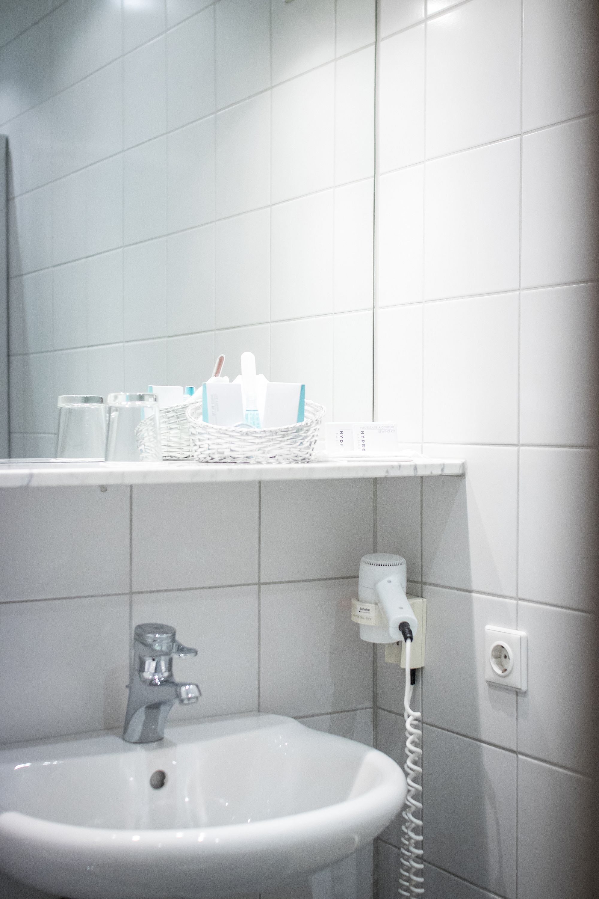 Un baño con un lavabo blanco, un espejo y una repisa con artículos de tocador.