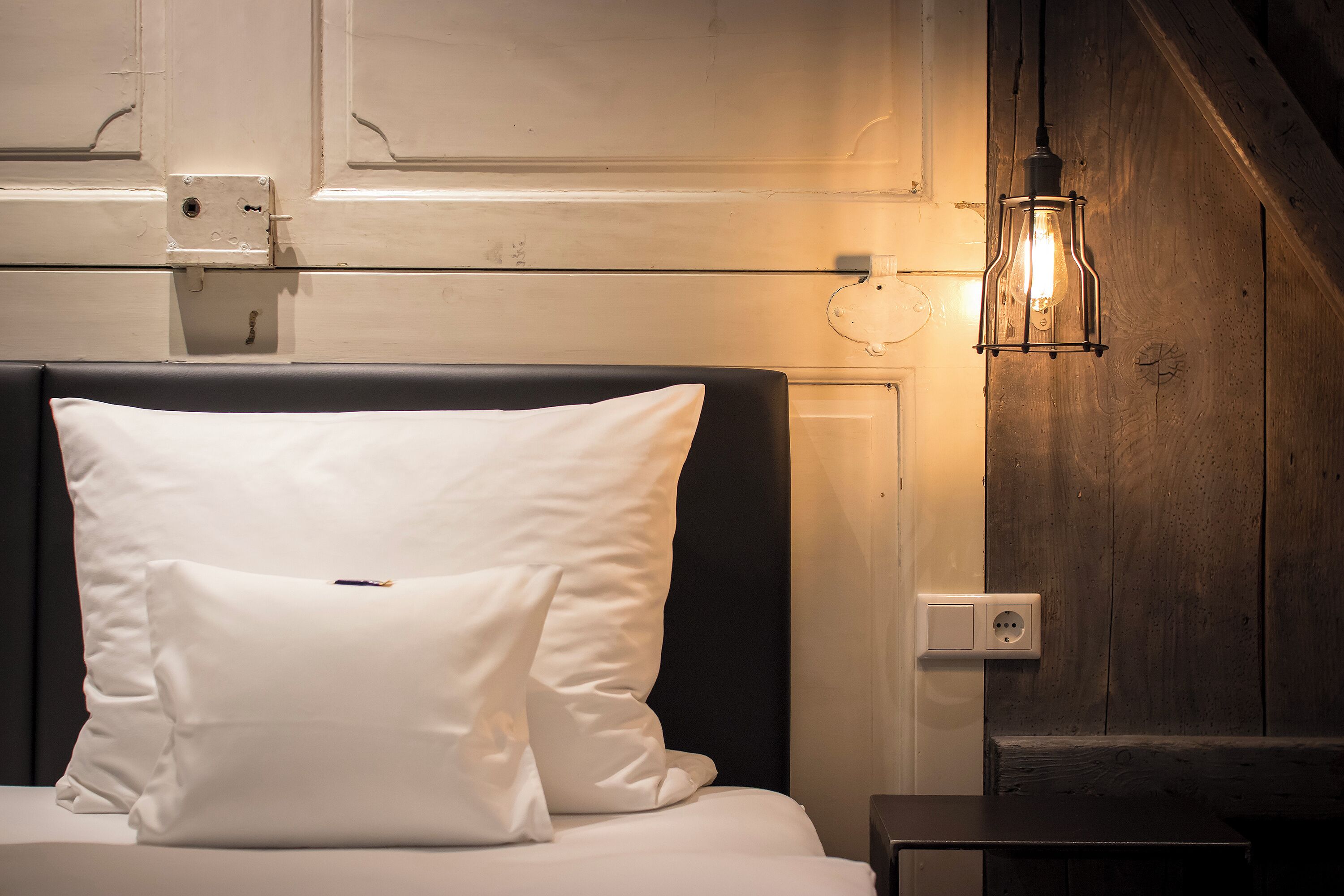 Een bed met witte kussens, een houten hoofdbord en een wandlamp.