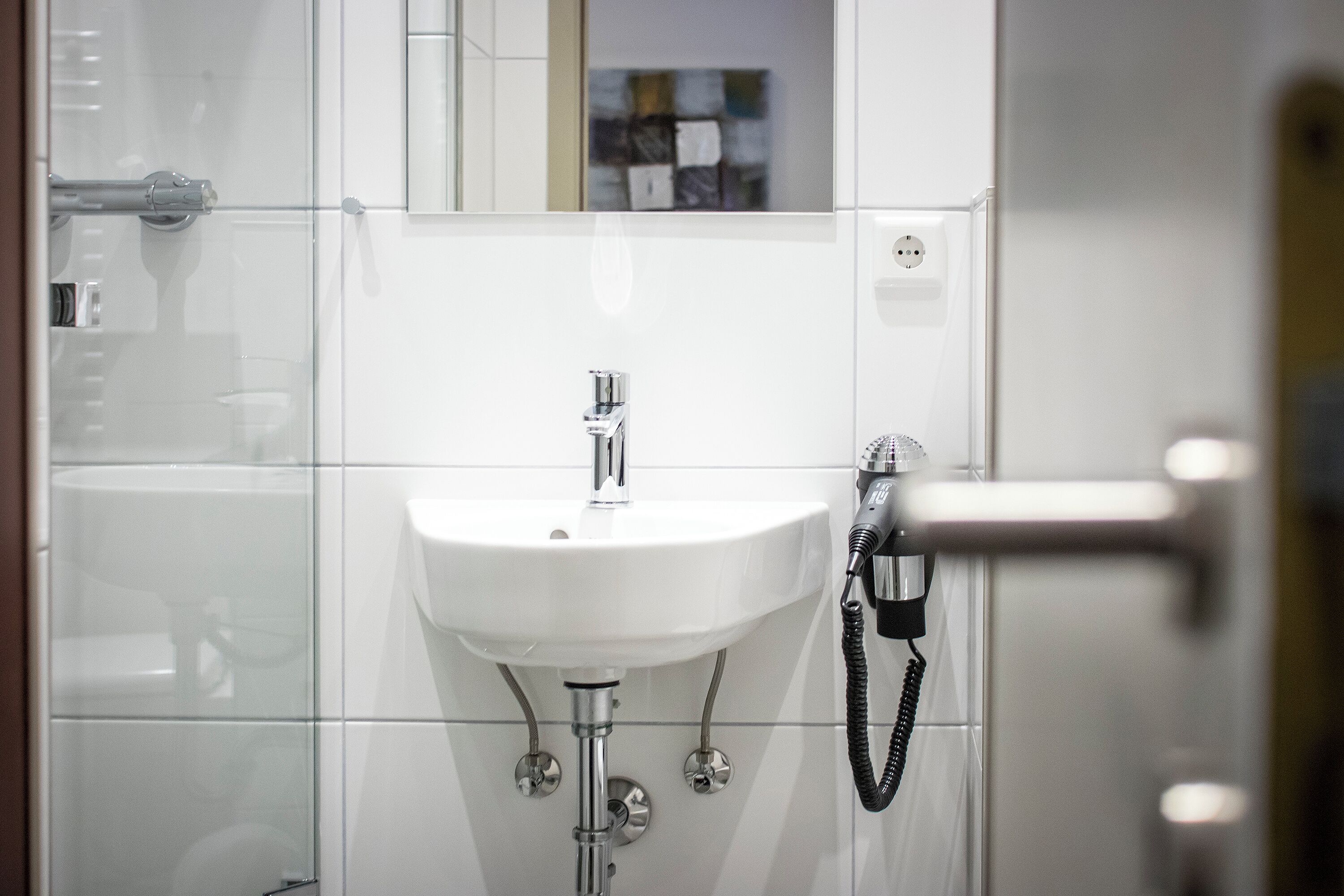 Un baño con lavamanos blanco, espejo y ducha.