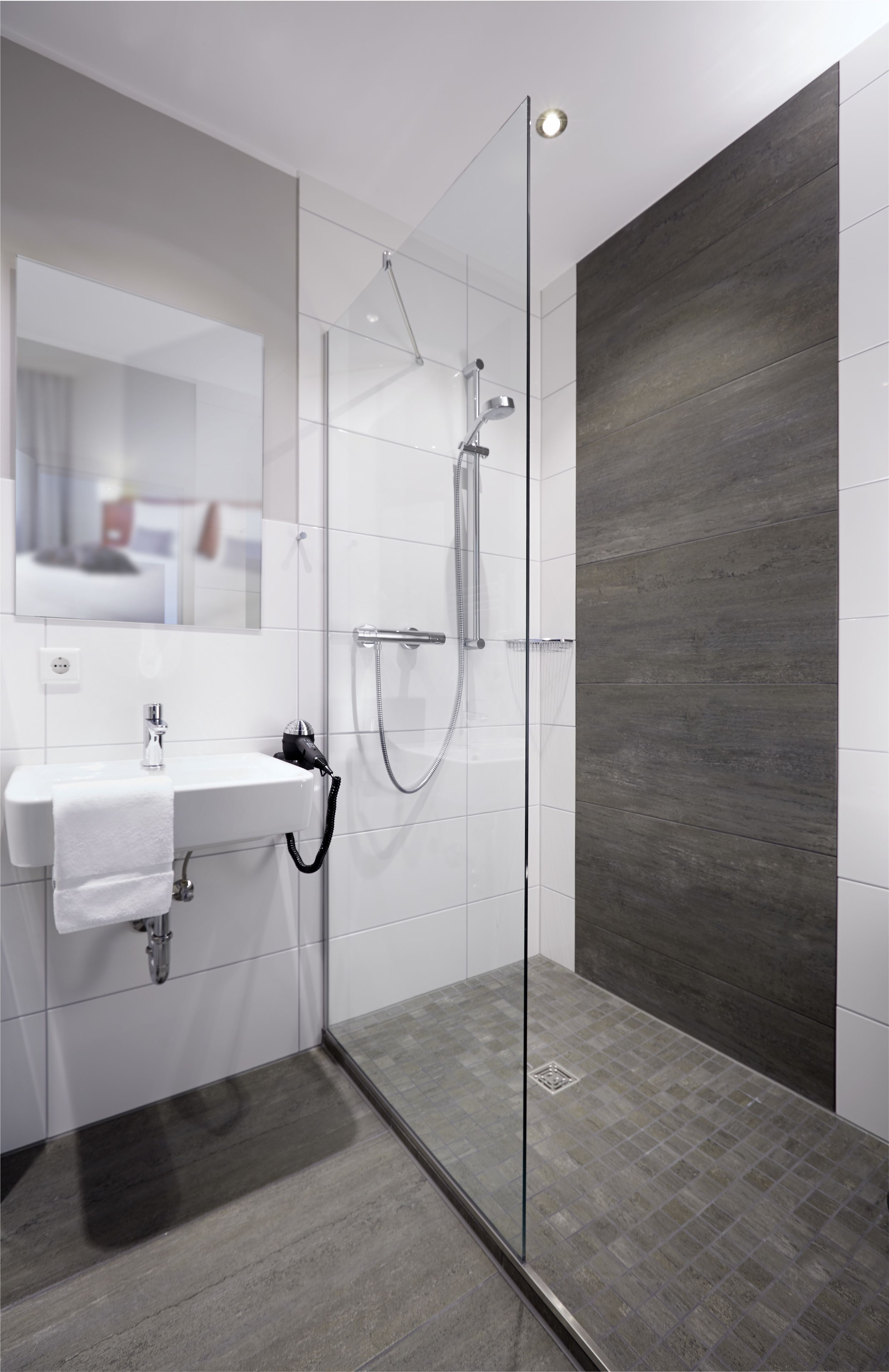 Un baño moderno con ducha envuelta en vidrio, lavamanos blanco y un panel de pared de madera oscura.