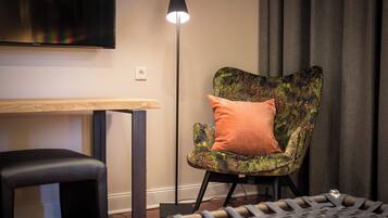 Une pièce moderne avec un fauteuil en cuir noir, une table en bois, un lampadaire et un pouf à motifs.