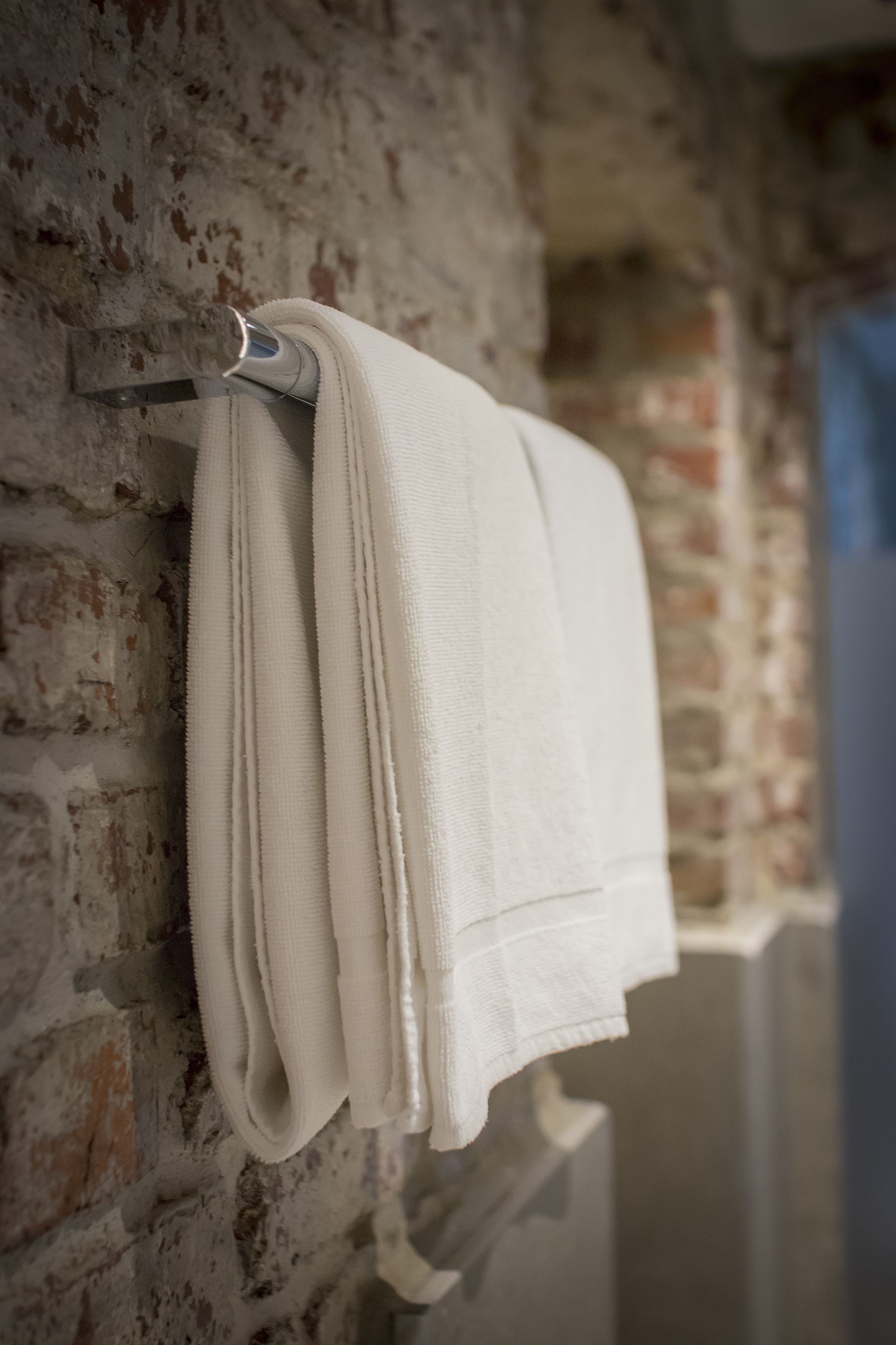 A white towel hanging on a metal towel rack attached to a brick wall.