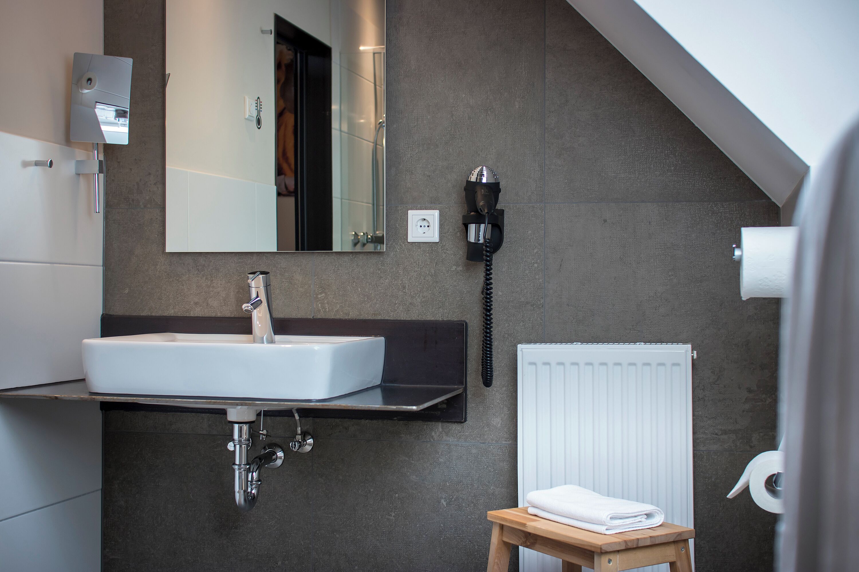 Un baño moderno con un lavamanos grande, un espejo, un perchero para toallas y una ducha.