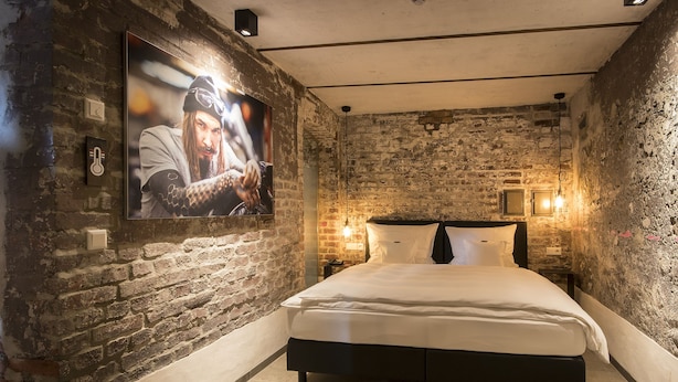 Une chambre avec un mur en briques, un lit, un téléviseur fixé au mur et deux lampes murales.