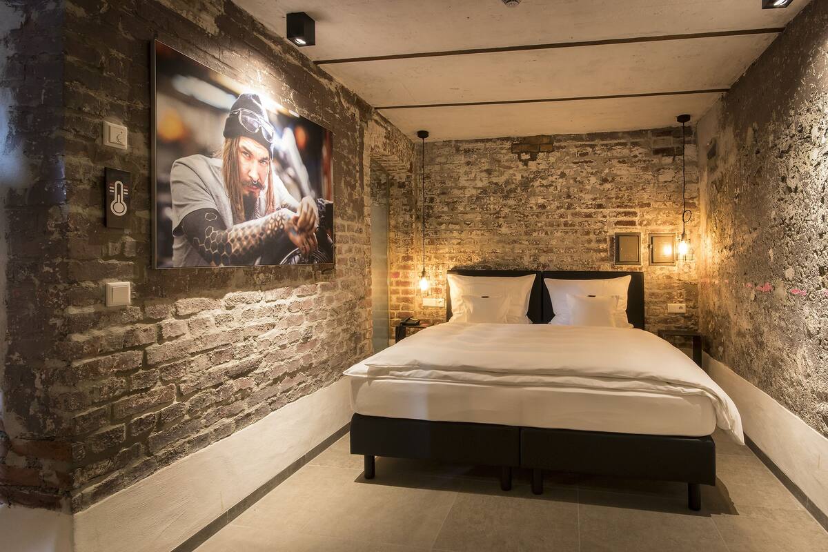 A bedroom with a brick wall, a bed, a mounted TV, and two wall-mounted lights.