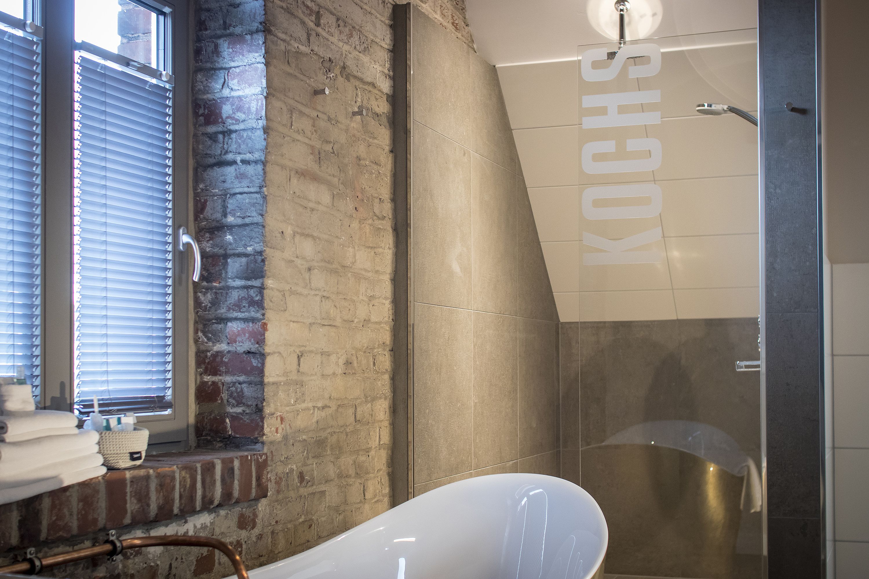 Ein modernes Badezimmer mit Backsteinwand, einer weißen Badewanne und einer Duschkabine.