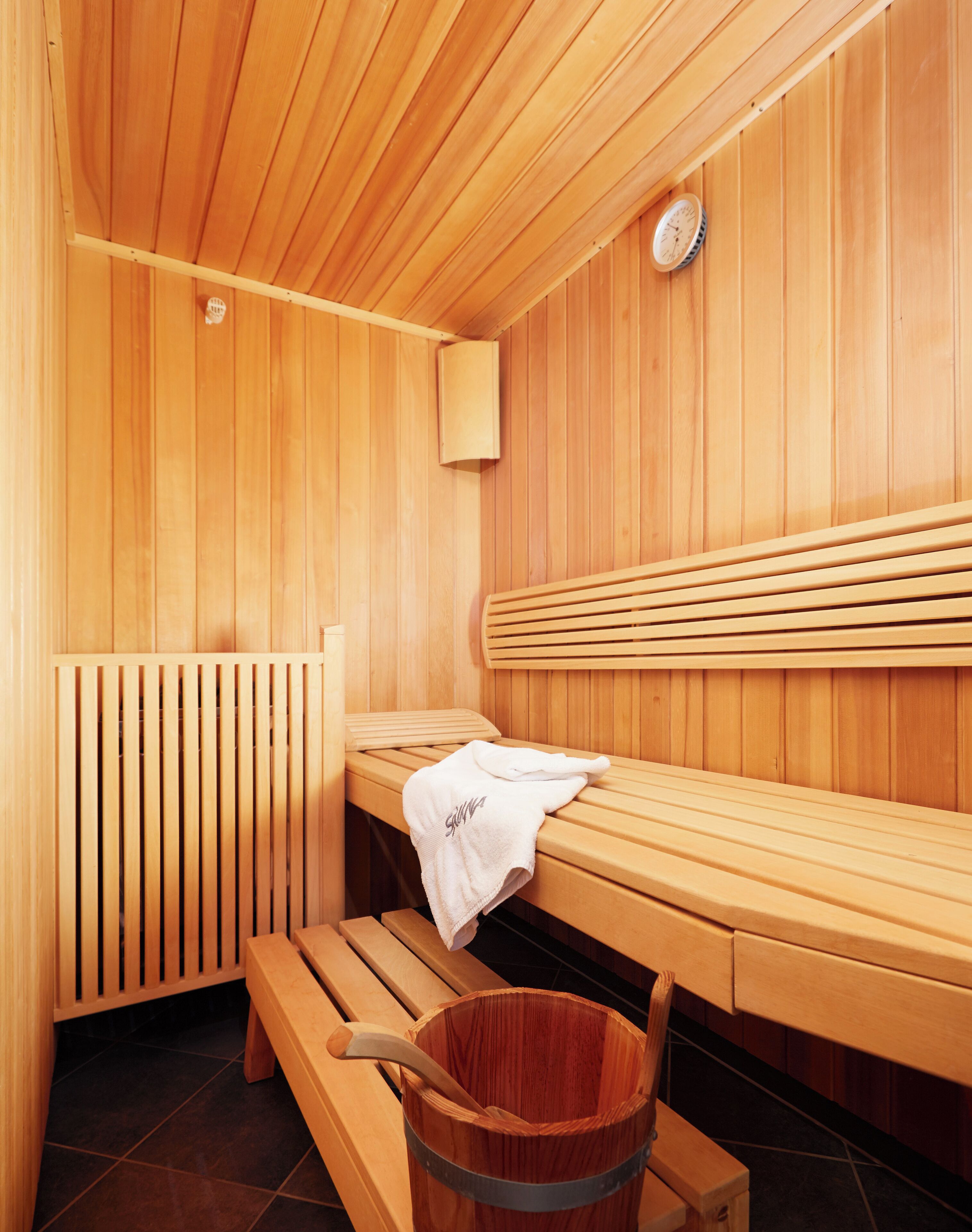 A sauna with wooden benches, a bench with a towel, and a bucket.