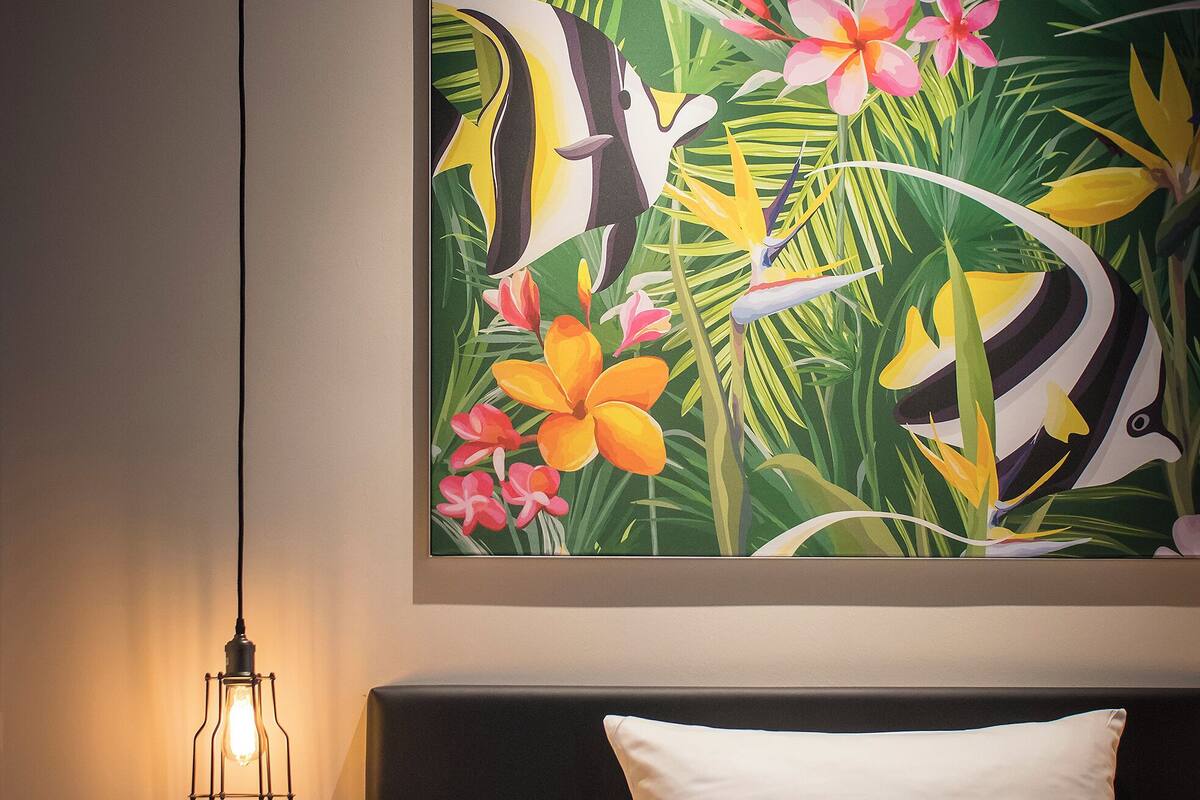 A hotel room with a bed, a nightstand, a lamp, and a tropical-themed wall mural.