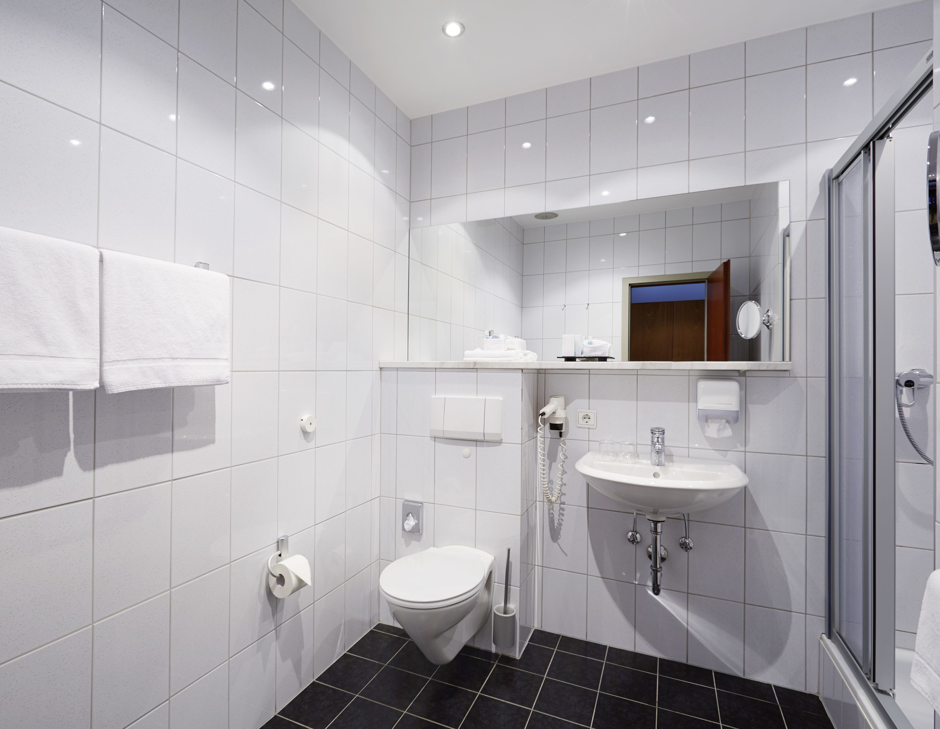 Une salle de bain moderne avec des carreaux blancs, des toilettes, un lavabo et une douche.