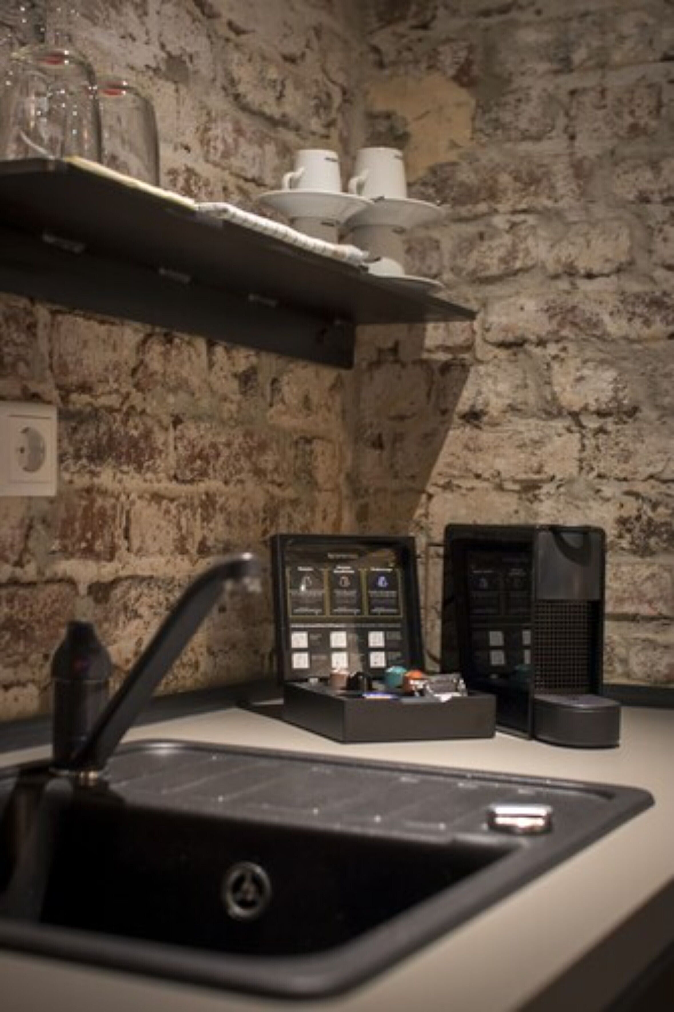 A kitchen with a stone wall, a sink, and a coffee machine.