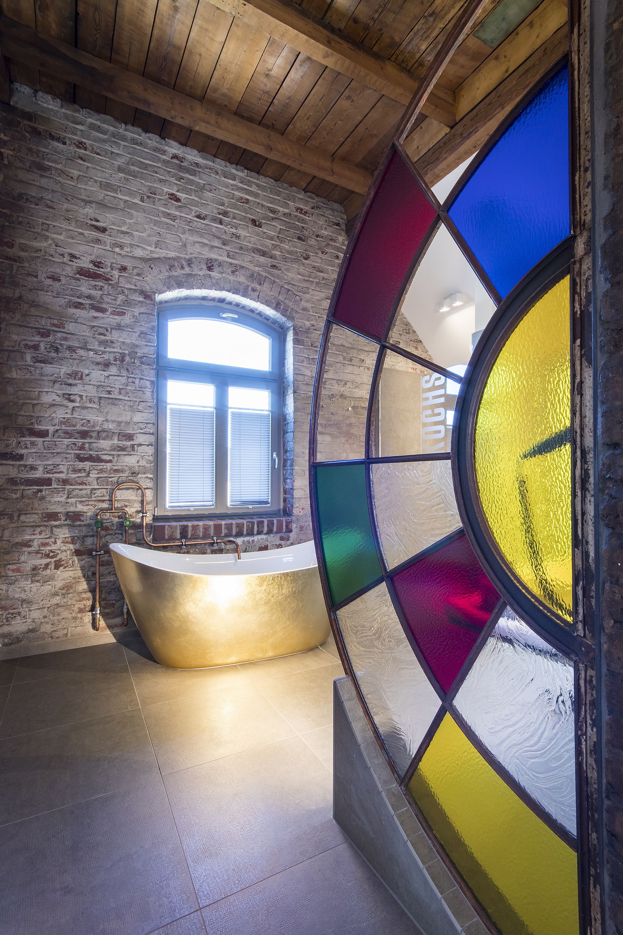 A room with a brick wall, a bathtub, and a stained glass window.