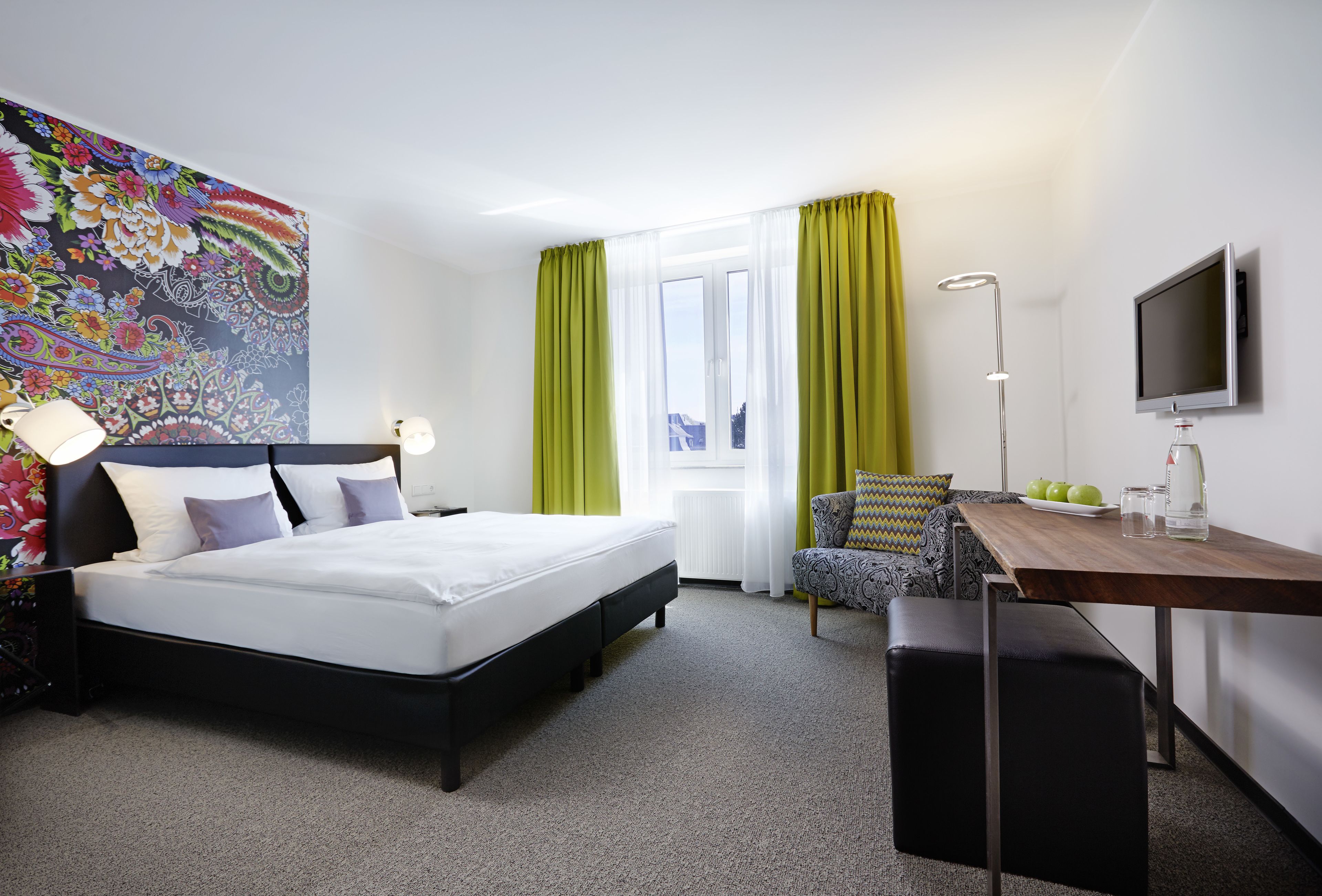 A hotel room with a bed, a desk, a chair, a TV, and a window with curtains.