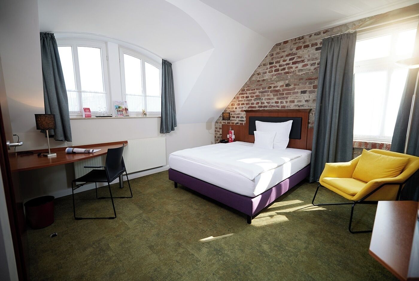 Habitación de hotel con cama, escritorio, silla y pared de ladrillo.