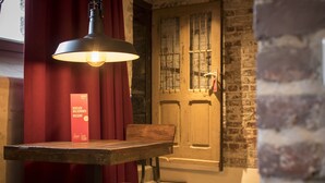 Une table en bois avec un banc, un luminaire suspendu, un rideau rouge et une porte en bois avec une fenêtre.