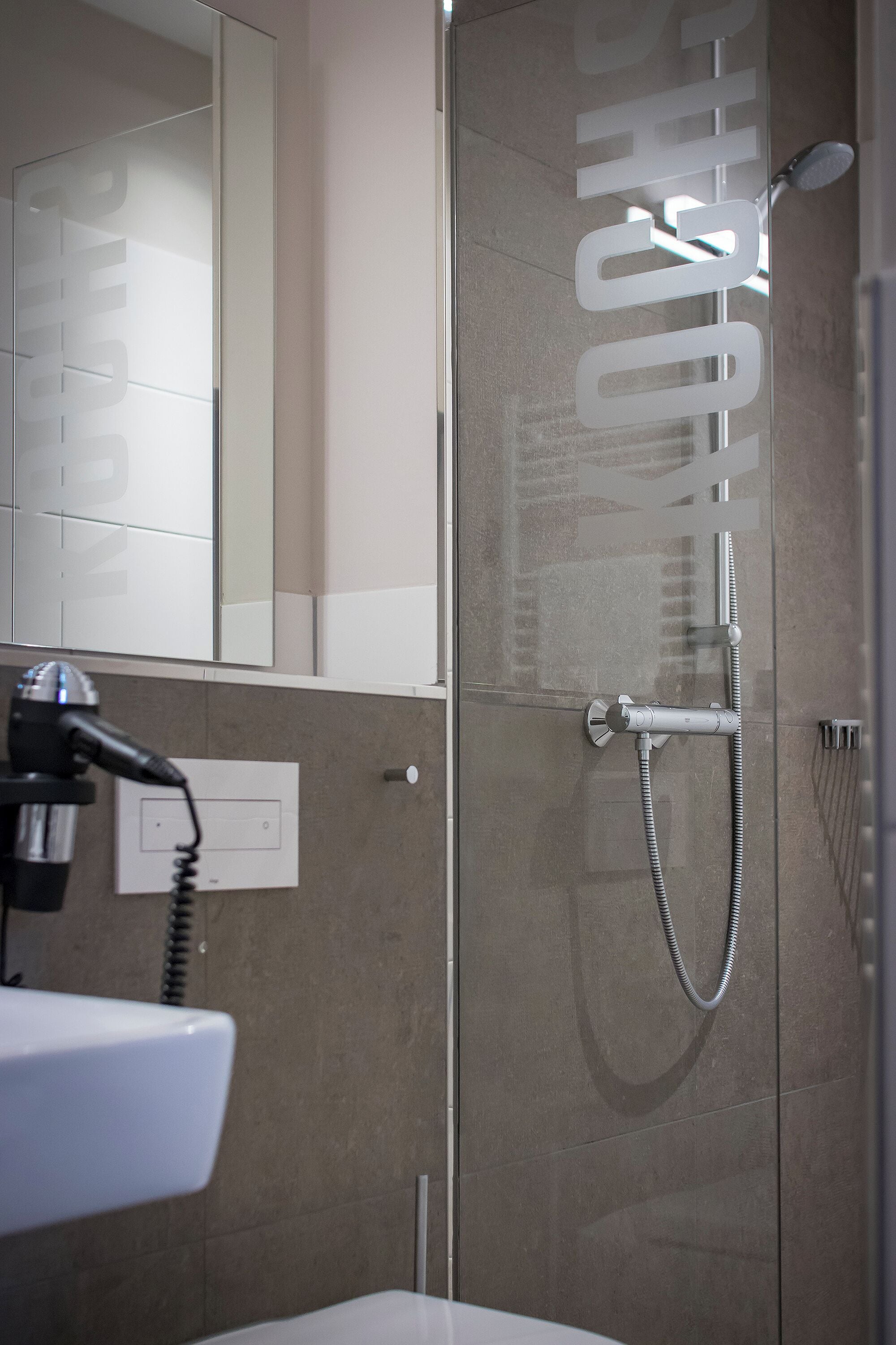 Un baño moderno con cabina de ducha de vidrio, ducha de mano y secador de pelo incorporado.