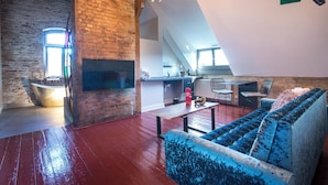 Un loft spacieux avec de hauts plafonds, des murs en briques apparentes, une cuisine moderne et un coin salon confortable avec un canapé bleu.