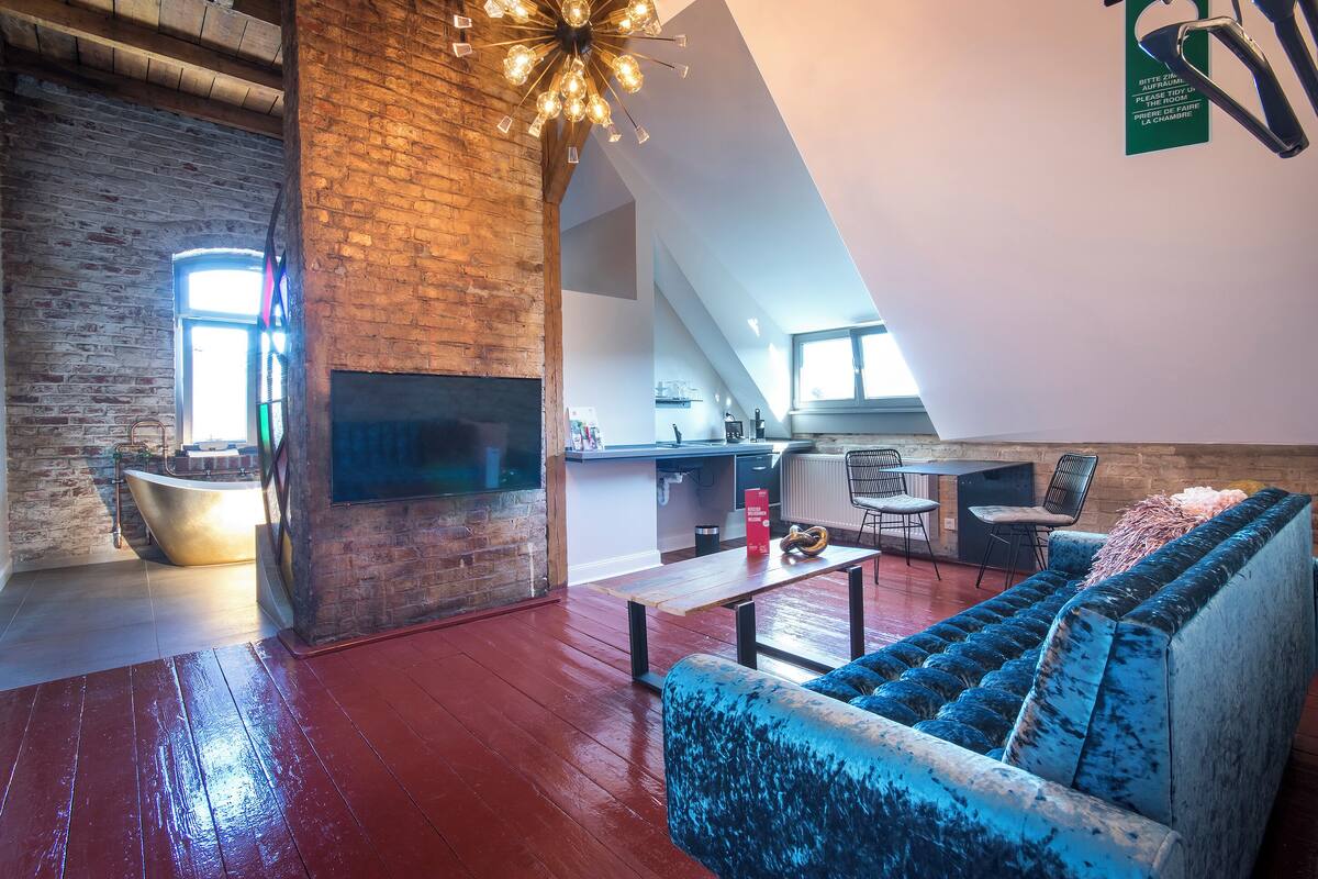 A spacious loft with a high ceiling, exposed brick walls, a modern kitchen, and a cozy seating area with a blue sofa.