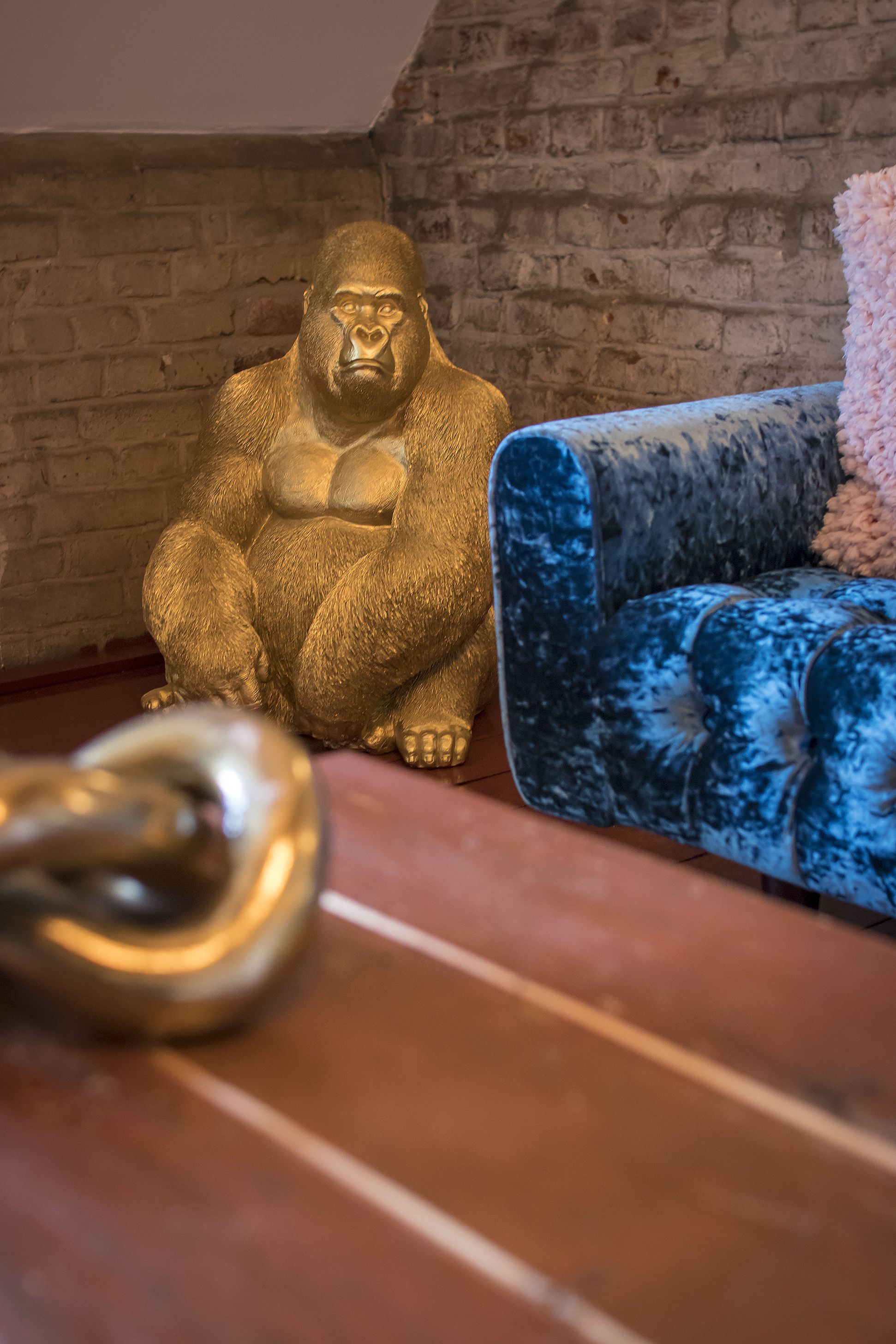 A room with a brick wall, a blue velvet sofa, and a golden statue.