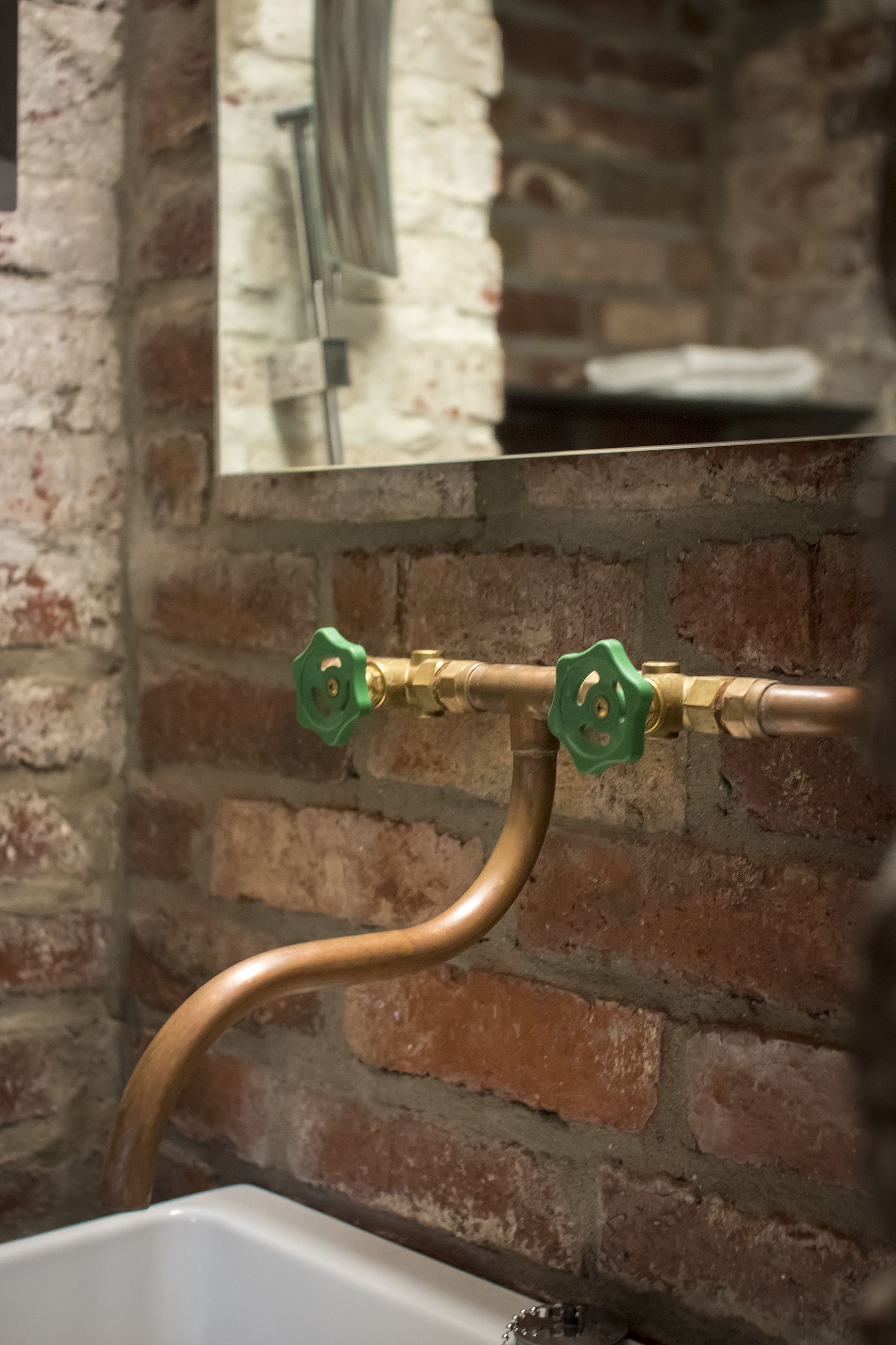 A bathroom with a brick wall, a white sink, and a green faucet.