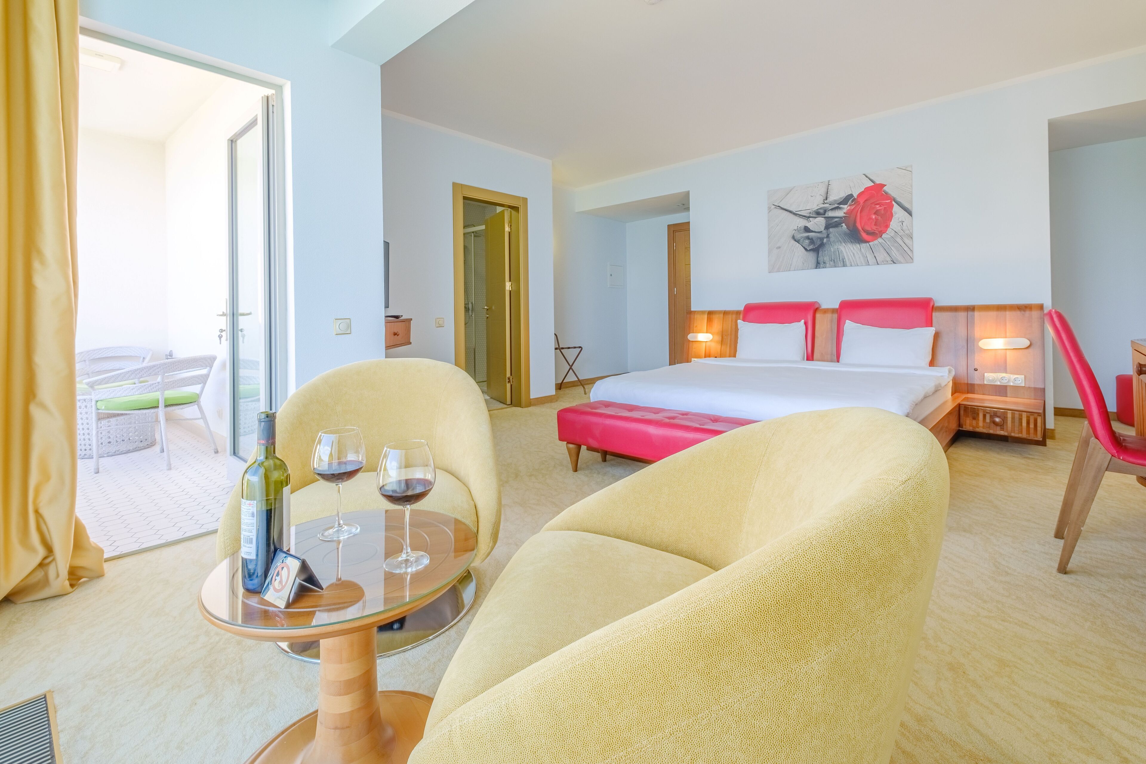 A hotel room with a bed, two armchairs, a small table with a wine bottle and glass, and a painting on the wall.