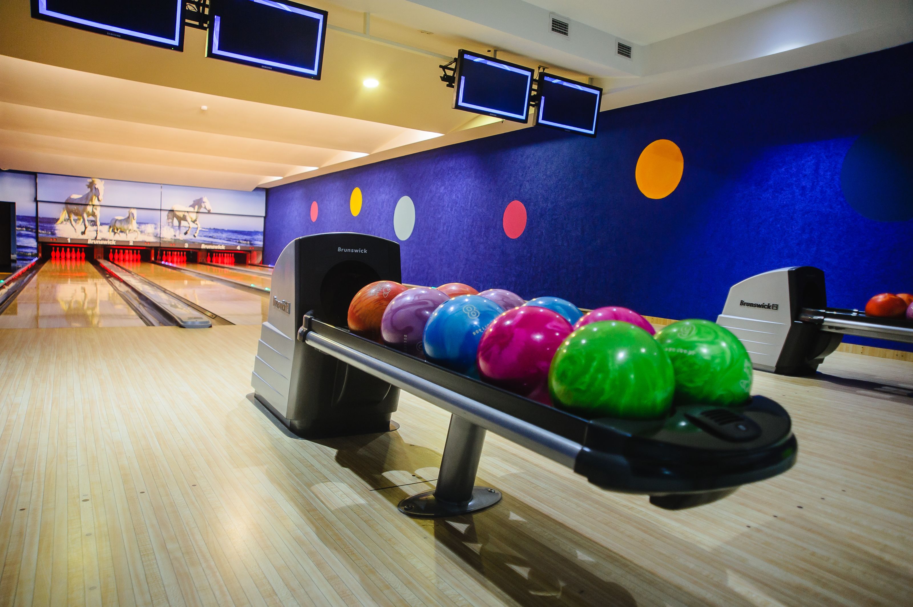 Une salle de bowling dotée de plusieurs pistes, d’un système de retour automatique des boules et d’un mur décoré de motifs circulaires colorés.