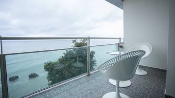 A balcony with a glass railing, two white chairs, and a view of the sea and trees.
