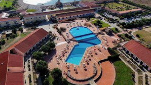Vue aérienne d’un complexe hôtelier doté d’une grande piscine centrale, de plusieurs bâtiments et d’une zone de plage.