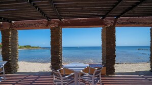 Un espace extérieur abrité, doté de piliers en pierre, offrant une vue sur une plage et la mer.