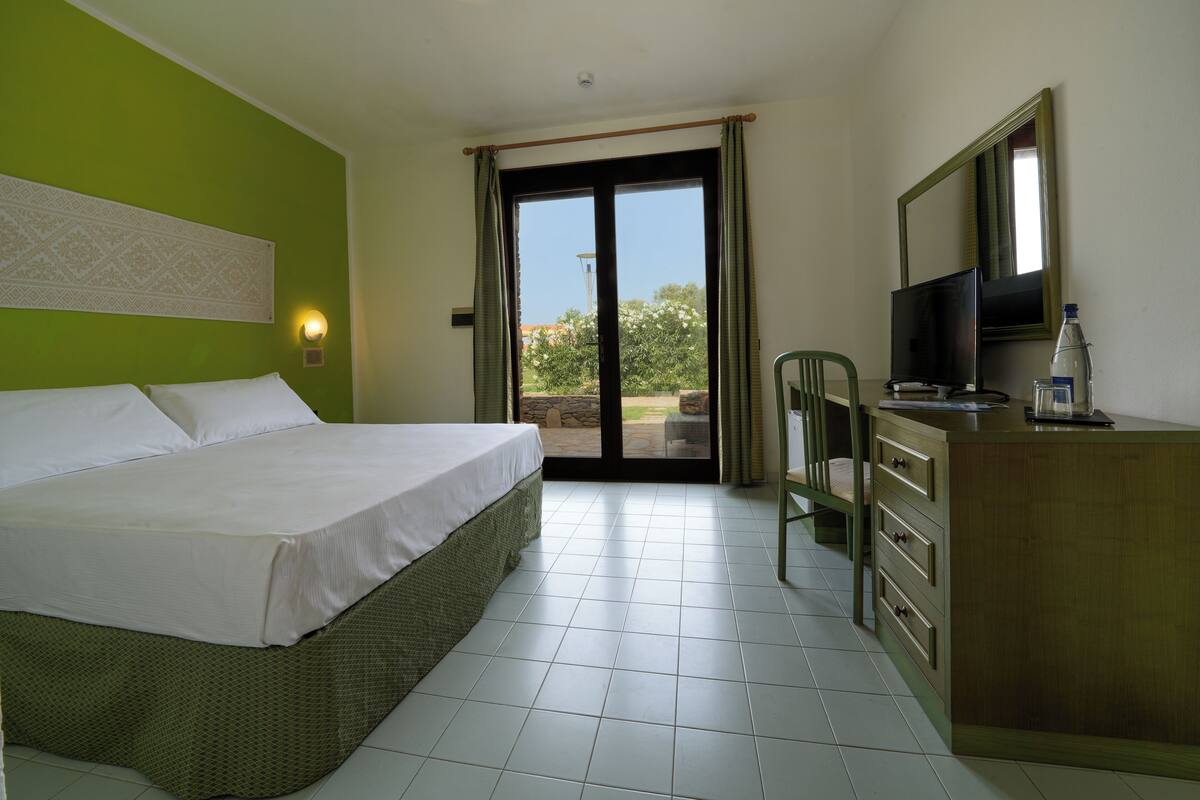 Een hotelkamer met een bed, een bureau met een televisie, een stoel en uitzicht op het omliggende landschap.