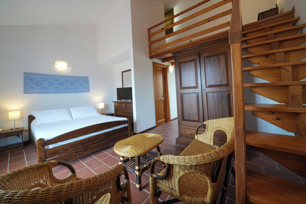 Een slaapkamer met een bed, nachtkastje, dressoir, stoel, tafel, spiegel en een houten trap.