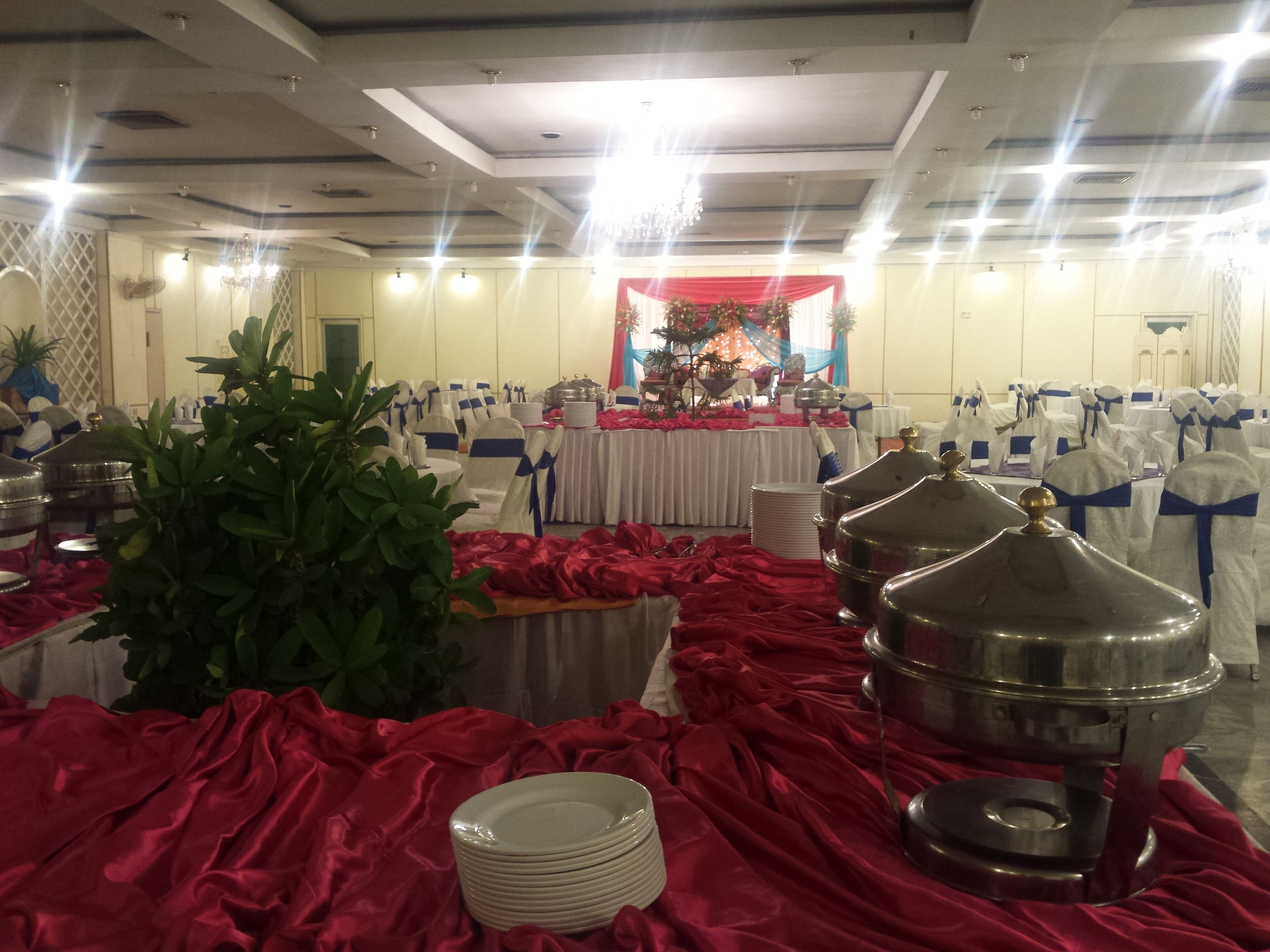 A banquet hall with round tables covered in white tablecloths, red drapes, and silver serving dishes.