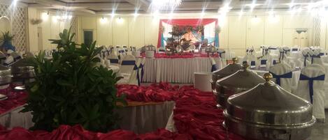 A banquet hall with round tables covered in white tablecloths, red drapes, and silver serving dishes.