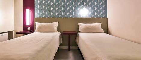 Habitación de hotel con dos camas individuales, una mesita de noche con lámpara y un muro con diseño de cactus.
