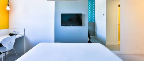 A modern hotel room with a bed, a desk, and a TV.