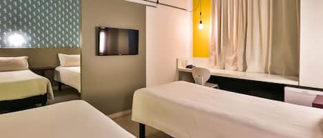 A hotel room with two beds, a desk, a chair, a TV, and a window with curtains.