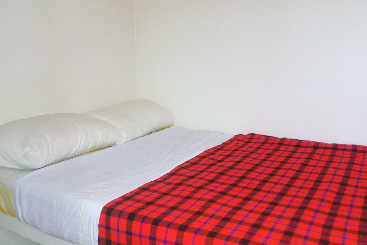 A single bed with white bedding and a red and black checkered blanket.