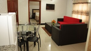 A modern living room with a glass dining table, black chairs, a red sofa, and a television mounted on the wall. - Sinai Suites Hotel (Kigali)