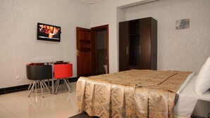 A hotel room with a bed, a desk with chairs, a wardrobe, and a television on the wall. - Sinai Suites Hotel (Kigali)