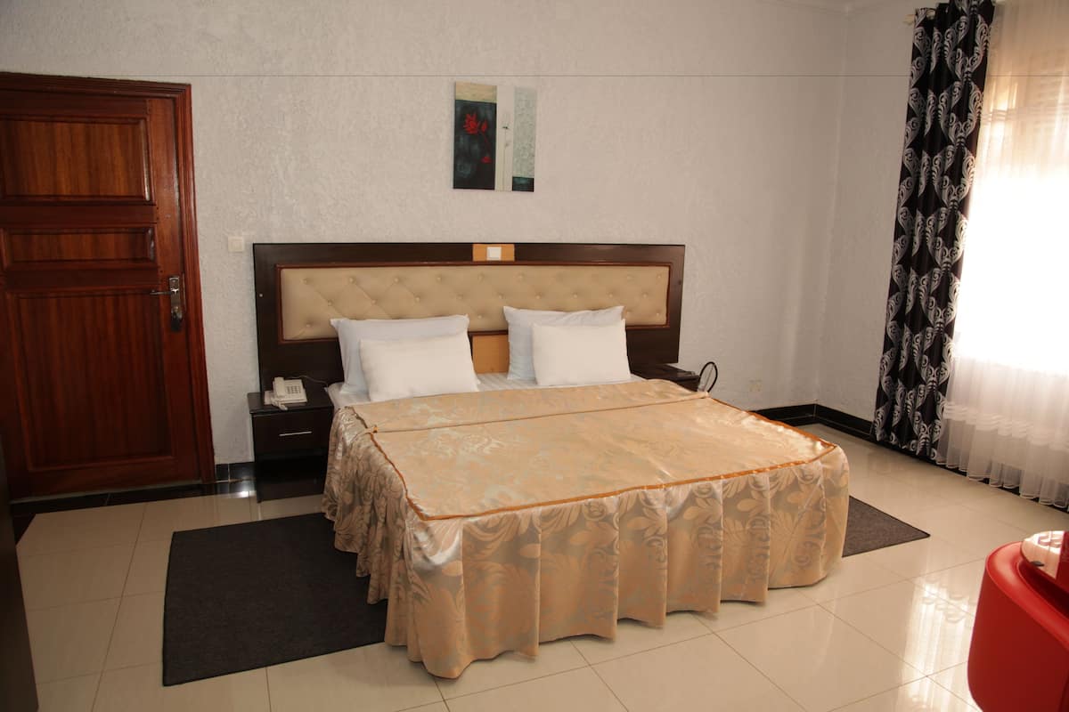 A hotel room with a large bed, a wooden door, a nightstand, and a red chair.