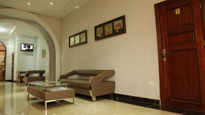 A lobby with a brown sofa, a glass coffee table, and a wooden door. - Sinai Suites Hotel (Kigali)
